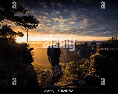 Dramatischer Sonnenaufgang über Sandsteinklippen mit glühenden Wolken und nebeligen Tälern. Stockfoto