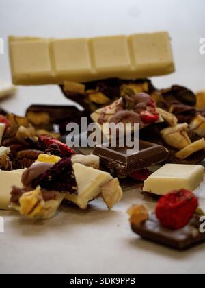 Verschiedene Schokoladenstücke gemischt mit getrockneten Früchten und Nüssen in einem kreativen, verstreuten Arrangement. Stockfoto