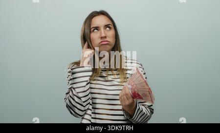 Frau, die isländische Kronen-Banknoten mit durchdachtem Ausdruck vor isoliertem weißem Hintergrund hält, was auf finanzielle Entscheidungen oder Geld hindeutet Stockfoto