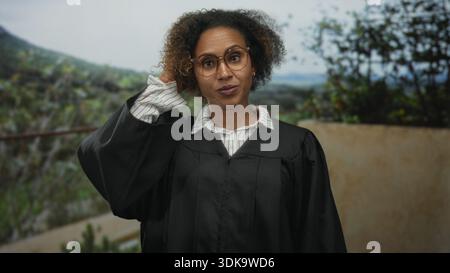 Eine Richterin im Gewand mit Brille hebt die Hand und berührt die Haare auf der Terrasse des Gebäudes im Freien; Skepsis ist weinend. Stockfoto