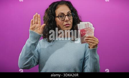 Frau, die isländische Kronen-Banknoten vor einem leuchtend violetten Hintergrund hält und damit finanzielle Verpflichtungen oder Versprechen symbolisiert. Stockfoto