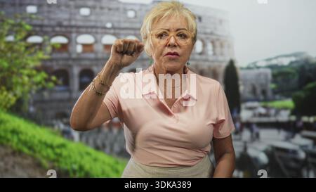 Seniorin zeigt mit den Fingern und zuckt mit den Händen vor das historische Gebäude; Verwirrungsfragen. Stockfoto