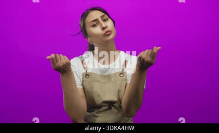 Frau mit Schürze und weißem Hemd lockt mit beiden Händen und zeigenden Fingern im magentafarbenen Atelier; Befragung. Stockfoto