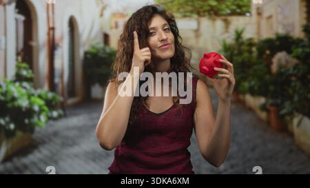 Die Frau zeigt mit dem Finger auf den Tempel, während sie auf der Kopfsteinpflasterstraße die rote Schweinebank hält. Stockfoto