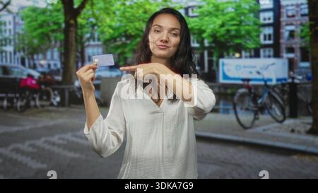 Die Frau zeigt mit dem Finger auf die Kreditkarte, während sie sie auf einer Stadtstraße am Kanal und an Fahrrädern hält; intelligentes Ausgabenvertrauen. Stockfoto