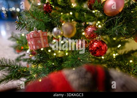 Ein festlicher Weihnachtsbaum steht drinnen, dekoriert mit kleinen hängenden Geschenkboxen, glänzenden Kugeln und warmen Lichtern, die sanft funkeln Stockfoto