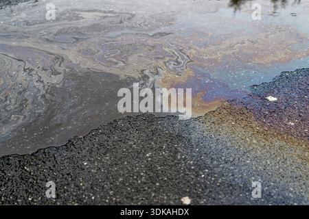 Eine flache Pfütze auf dunklem Asphalt zeigt dicke Ölrückstände und Treibstoffglanz, die Regenbogenwirbel bilden, die sich nach dem Passieren von t über die nasse Straßenoberfläche ausbreiten Stockfoto