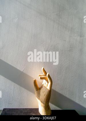 Nahaufnahme einer hölzernen Handskulptur, beleuchtet von hellem Sonnenlicht vor einem rauen grauen strukturierten Hintergrund, Kunstkonzept und Hoffnung. Stockfoto