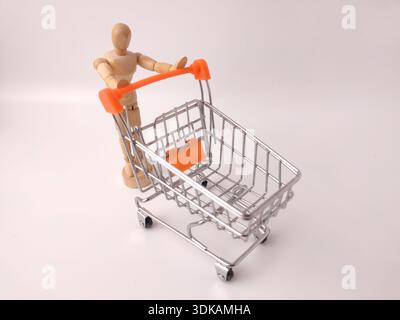 Eine Holzpuppe, die einen Miniatur-Einkaufswagen aus Metall schiebt. Stockfoto
