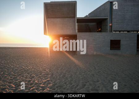 Eine architektonische Nahaufnahme eines brutalistischen Betongebäudes am Strand, mit einem dramatischen Sonnenaufgang und einem Lichtstrahl um die Ecke Stockfoto