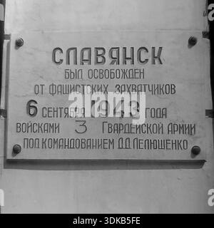 Slawjansk, Ukrainische SSR, Sowjetunion, 1960er Jahre Ein Archivfoto, das eine Nahaufnahme einer Gedenktafel zeigt, die der Befreiung der Stadt gewidmet ist. Die Inschrift lautet: „Slawansk wurde am 6. September 1943 von den Truppen der 3. Garde unter dem Kommando von D.D. Leljuschenko von faschistischen Eindringlingen befreit.“ Die Gedenktafel ist an der hell verputzten Wand eines Schulgebäudes angebracht. Dieses Bild dokumentiert das historische Gedächtnis und die Ehren der Ereignisse des Zweiten Weltkriegs in der friedlichen Donbass-Region. Stockfoto
