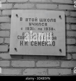 Slawjansk, Ukrainische SSR, Sowjetunion, 1960er Jahre Ein Archivfoto mit einer Nahaufnahme einer Gedenktafel an der weißen Ziegelwand der Schule Nr. 12. Die Inschrift erinnert an Nikolai Illarionowitsch Semeyko, einen zweifachen Helden der Sowjetunion, der besagt, dass er an dieser Schule von 1931 bis 1938 studierte. Die einfache und dennoch würdevolle Gedenktafel ehrt die Erinnerung an den berühmten Piloten und Kriegshelden. Dieses Bild spiegelt die Erhaltung des historischen Erbes und der patriotischen Werte in den Bildungseinrichtungen des friedlichen Donbass wider. Stockfoto