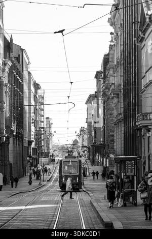 Schwarz-weiße Straßenszene mit einer Straßenbahn, die durch eine geschäftige urbane Straße in Helsinki, Finnland, fährt und den Alltag und die Architektur der Stadt zeigt. Stockfoto