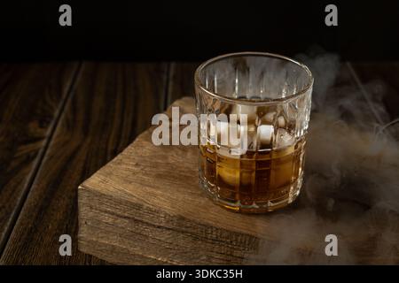Geräucherter altmodischer Cocktail in einem Kristallglas mit Orangenschalen auf einer rustikalen Holzoberfläche. Dunkle stimmungsvolle Atmosphäre mit Raucheffekt und Bric Stockfoto