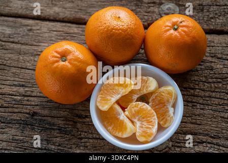 Mehrere Orangen Obst und Scheiben auf einem weißen Teller auf einem alten Holztisch Stockfoto