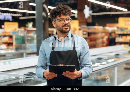 Mit Notizblock. Männlicher Arbeiter ist im Supermarkt. Stockfoto