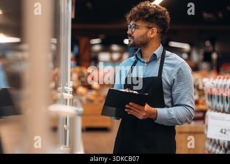 Mit Notizblock. Männlicher Arbeiter ist im Supermarkt. Stockfoto