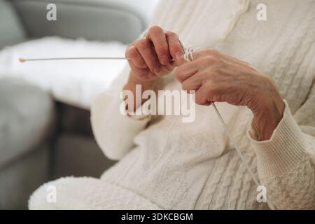 Nahaufnahme von Großmutter, die zu Hause auf einem Stuhl sitzt und strickt. Stockfoto