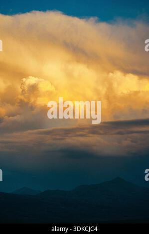 Glühende Sturmwolken, die vom Sonnenuntergang über dunklen Berglandschaften beleuchtet werden, schaffen eine dramatische und filmische Abendszene. Stockfoto