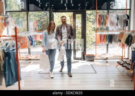 Positive Gesichtsausdrücke. Schwangere Frau mit Mann sind im Kinderbekleidungsgeschäft. Stockfoto