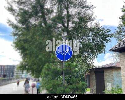 Rundes blaues Straßenschild mit Fußgänger und Fahrrad, verschwommener Fußgängerstraße und Radfahrern im Hintergrund Stockfoto