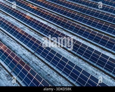 Von oben nach unten gerichtete Solarpaneele in diagonalen Reihen mit leichtem Schnee dazwischen. Starkes geometrisches Muster und abstrakte Hintergrundrepressionen Stockfoto