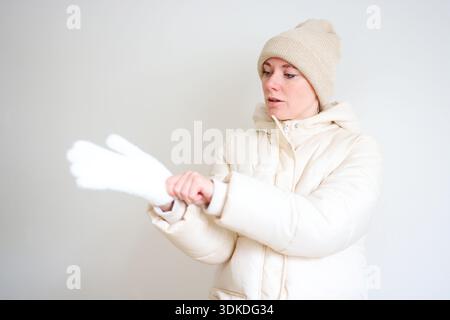 Lächelnde Frau, die warme Winterjacke Hut und Handschuhe auf hellem Hintergrund trägt Stockfoto