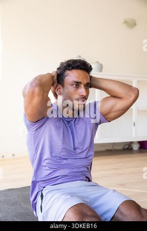 Ein Mann mit 20 Jahren, der Sportkleidung trägt und zu Hause mit Keramikvase Sit-up auf der Trainingsmatte macht. Fitness, Kraft, Wellness, Heimtrainer, Workout, Muskulatur, aktiver Lebensstil || Model veröffentlicht Stockfoto