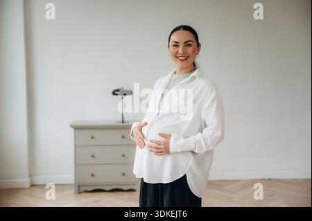 Schwangere Frau steht zu Hause im Wohnzimmer. Stockfoto