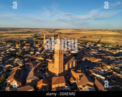 Luftaufnahme einer malerischen europäischen Stadt mit roten Ziegeldächern, zwei hohen Kirchtürmen und einer weiten Landschaft, die bei Sonnenuntergang leuchtet: Alaejos, Castile und Leon Stockfoto