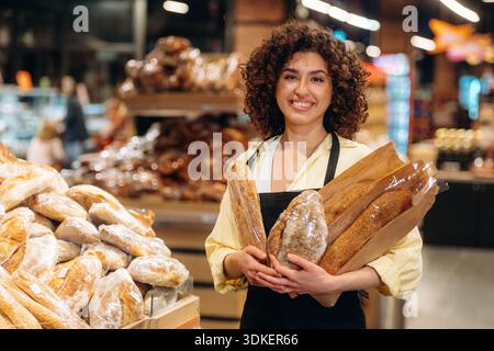 Eine Arbeiterin in Schürze ist mit Bäckerei in Händen, steht im Supermarkt. Stockfoto