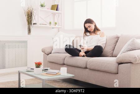 Frau im Haus, die online Nachrichten sendet, auf der Couch sitzt Stockfoto