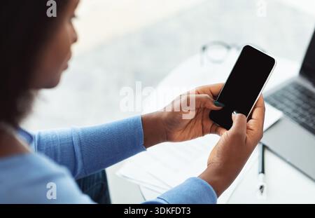 Rückansicht einer schwarzen Frau, die auf dem Sofa sitzt und das Telefon benutzt Stockfoto