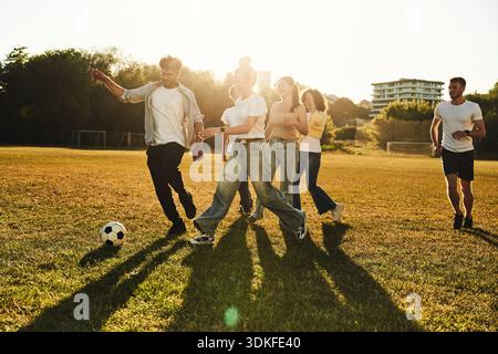 Gemeinsam laufen. Eine Gruppe von Freunden spielt Fußball auf dem Spielfeld. Stockfoto