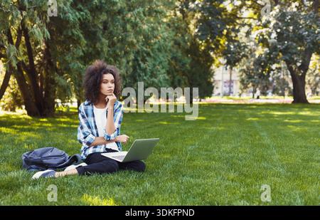 Ernste junge schwarze Frau, die im Park einen Laptop benutzt Stockfoto
