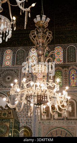 Monumentales Glas und Kristallleuchter in einer Fès-Madrasa, umgeben von zellige Fliesen, geschnitztem Stuck und fein farbigen traditionellen marokkanischen Färbungen Stockfoto