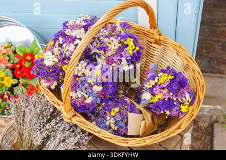 Helle getrocknete statice-, Kermek- oder Limonium-Blumensträuße im Korb im Blumengeschäft auf rustikalem hölzernem Terrassenhintergrund angeordnet, wodurch ein gemütliches Coun entsteht Stockfoto