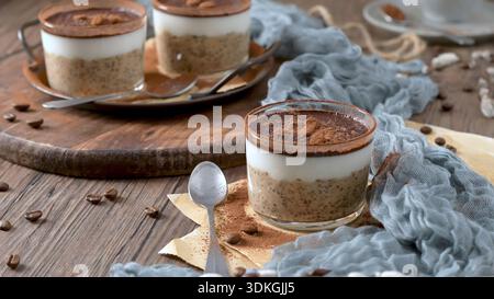 Eine rustikale Nahaufnahme gesunder mehrschichtiger Desserts in Glasbechern auf einem Holztisch. Weiches natürliches Licht hebt die cremige Textur der Chiasamen und hervor Stockfoto