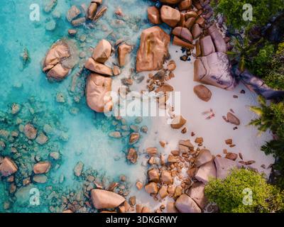 Kristallklares türkisfarbenes Wasser trifft auf glatten goldenen Sand am Grand Anse Beach in Praslin Seychellen. Entlang der Küste gesäumte Felsbrocken schaffen ein friedliches AT Stockfoto