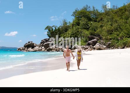 Das Paar genießt einen romantischen Spaziergang am weißen Sandstrand von Anse Georgette, umgeben von azurblauem Wasser und üppigem Grün. Praslin, Seychellen Stockfoto