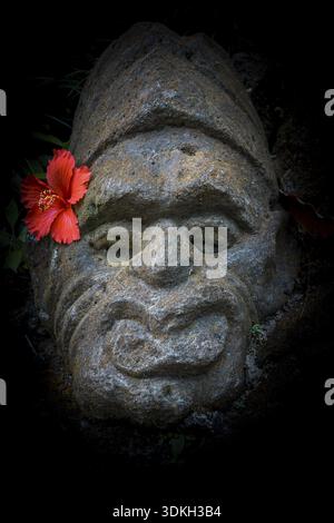 Alte balinesischer Stein mit einem roten Hibiskus Blume hinter dem Ohr, Ubud, Bali, April, 14 2018 Stockfoto