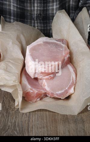 Essen, Ein Haufen frisch gehackter roher Schweinefleisch-Steaks über den Knochen in Geschenkpapier in den Händen eines Mannes Stockfoto