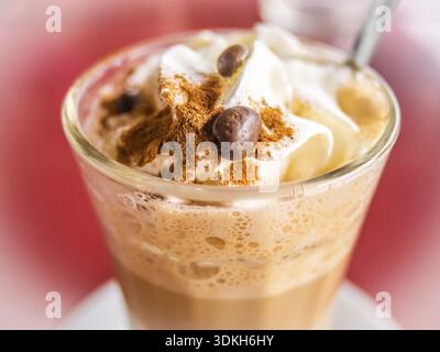 Kaffee Latte im Longdrinkglas mit geschlagener Sahne, Zimt und Kaffee Bohnen als Beilage Stockfoto