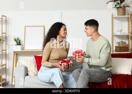 Liebevolles junges Paar, das zu Hause auf dem Sofa Geschenke austauscht. Valentinstag-Feier Stockfoto