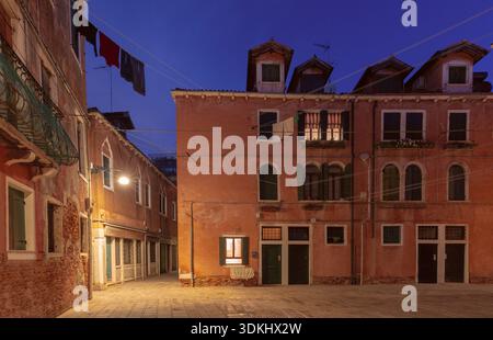 Eine ruhige Abendstraße in Venedig, Italien, mit traditionellen Häusern, warmen Lichtern und Wäscherei über der Gasse Stockfoto