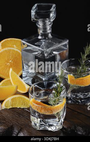 Essen, Cocktail klassischer Dry Gin mit Tonic und Orangenschale mit einem Zweig Rosmarin auf einem Holzbrett mit saftigen Orangenscheiben Stockfoto