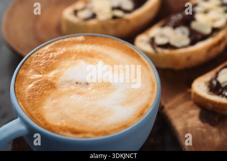 Frischer Cappuccino in blauer Tasse mit Toasts mit Schokoladenaufstrich Auf konkretem Hintergrund Stockfoto
