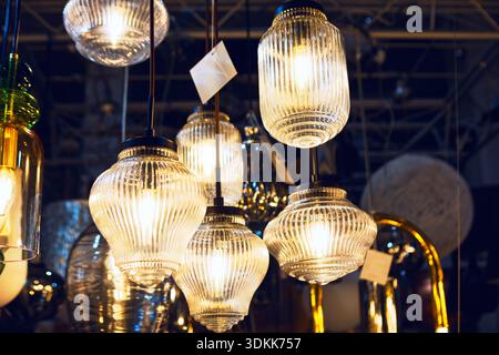 Die Pendelleuchten aus geripptem Glas leuchten im Showroom warm, wobei jede Leuchte subtile Variationen in Form und Größe aufweist Stockfoto