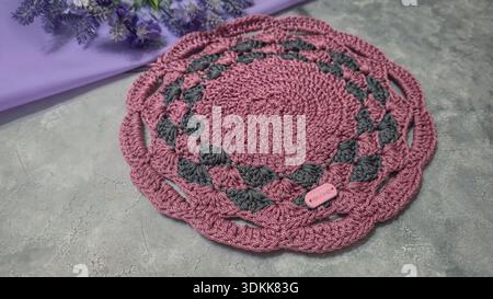 Gestrickte runde lilafarbene Tischsets auf grauem Hintergrund. Inneneinrichtung. Grüne Platten. Geeignet für Wohnkultur, Mode oder Textilhandwerk. Muster. Stockfoto