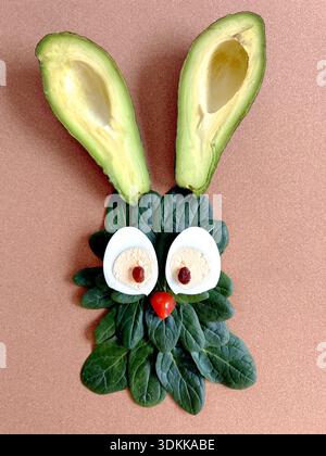 Ein verspieltes Hasengesicht aus Avocadohälften, Spinatblättern, gekochten Eiern und Tomaten als kreative Kunst für gesunde Lebensmittel Stockfoto